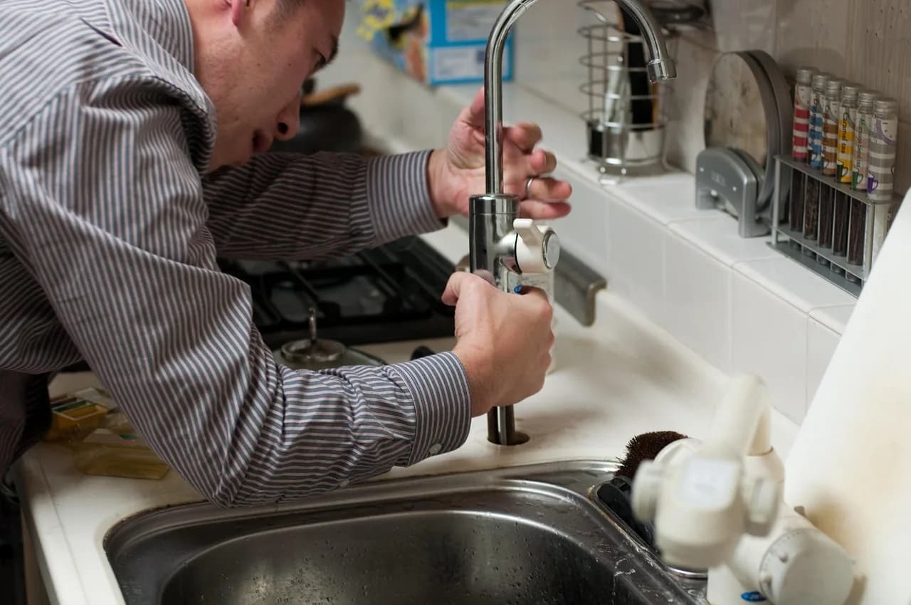 Professional plumber repairing pipes beneath a kitchen sink